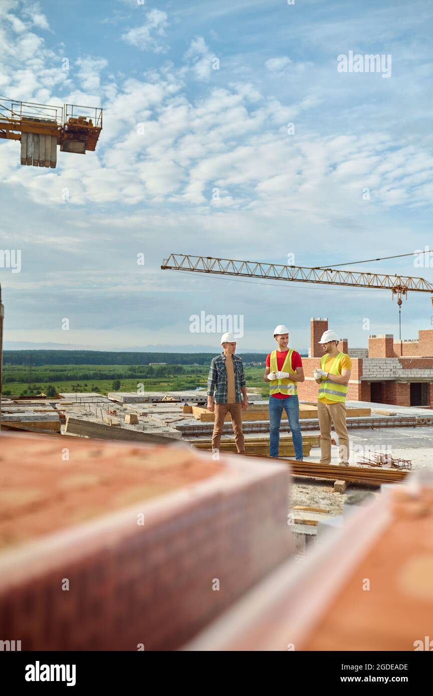 Three men in protective helmets standing on the building site Stock Photo
