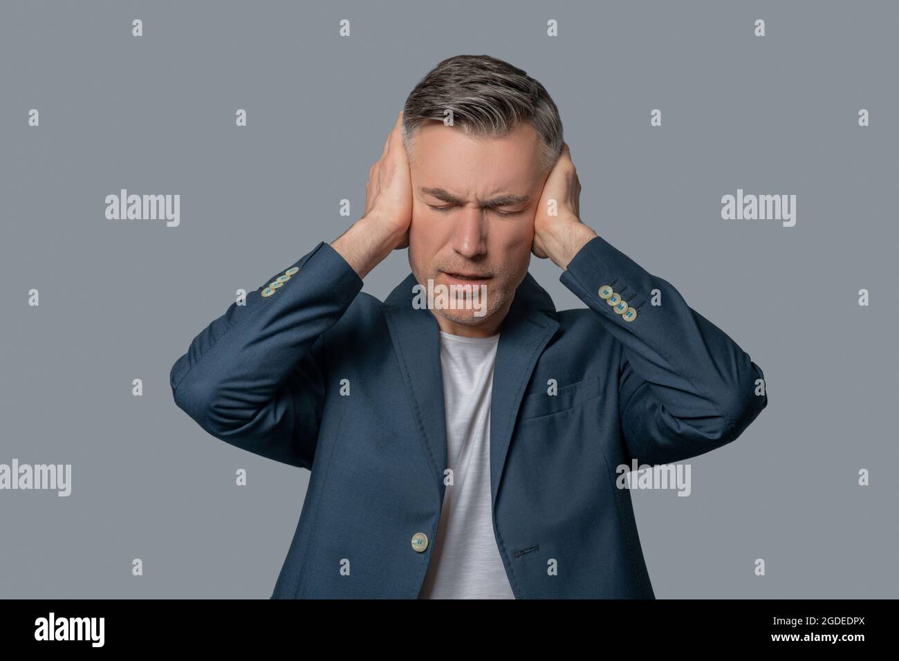 Man with drooping eyelids covering ears with hands Stock Photo