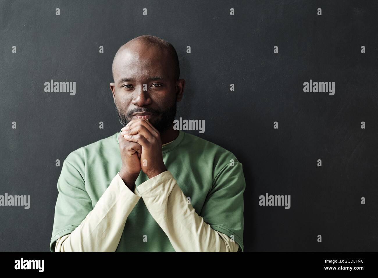 Portrait of African pensive man looking at camera standing against the black background Stock Photo