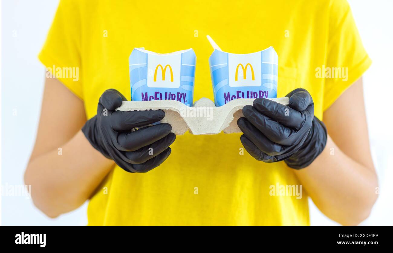 Woman in a yellow t-short holding an ice cream Mcflurry in medical gloves. Delivery McCafe. fast food restaurant Mcdonalds. ake away ice cream Stock Photo