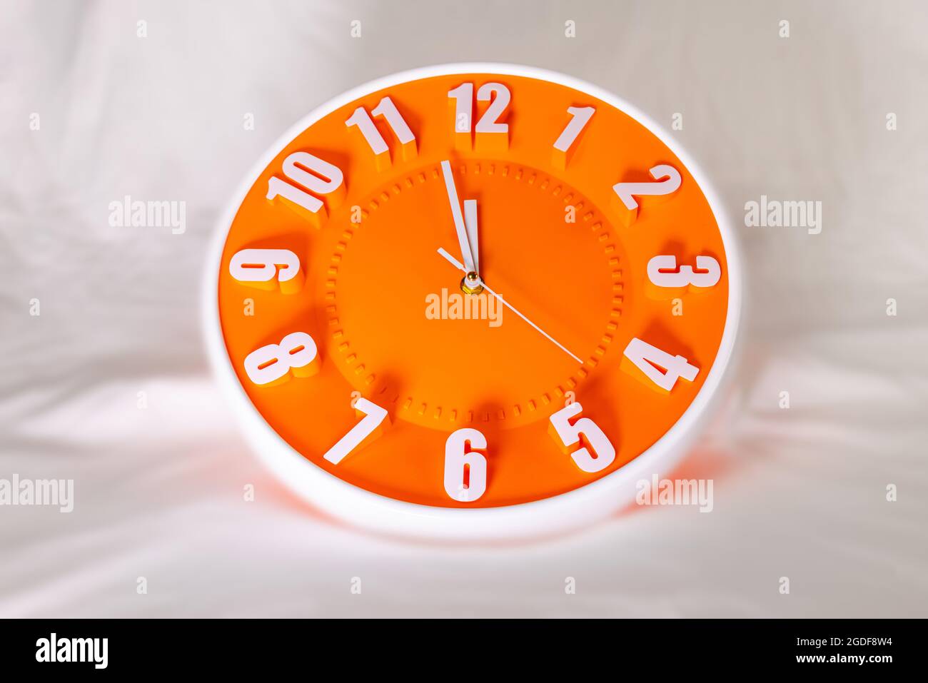 Orange clock face of a wall clock show the time. It's close to 12 o'clock. The latest report of the atomic scientist shows the doomsday clock Stock Photo
