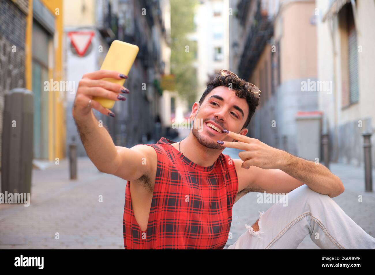 Young caucasian man with long false nails taking a selfie sitting on the floor. Stock Photo