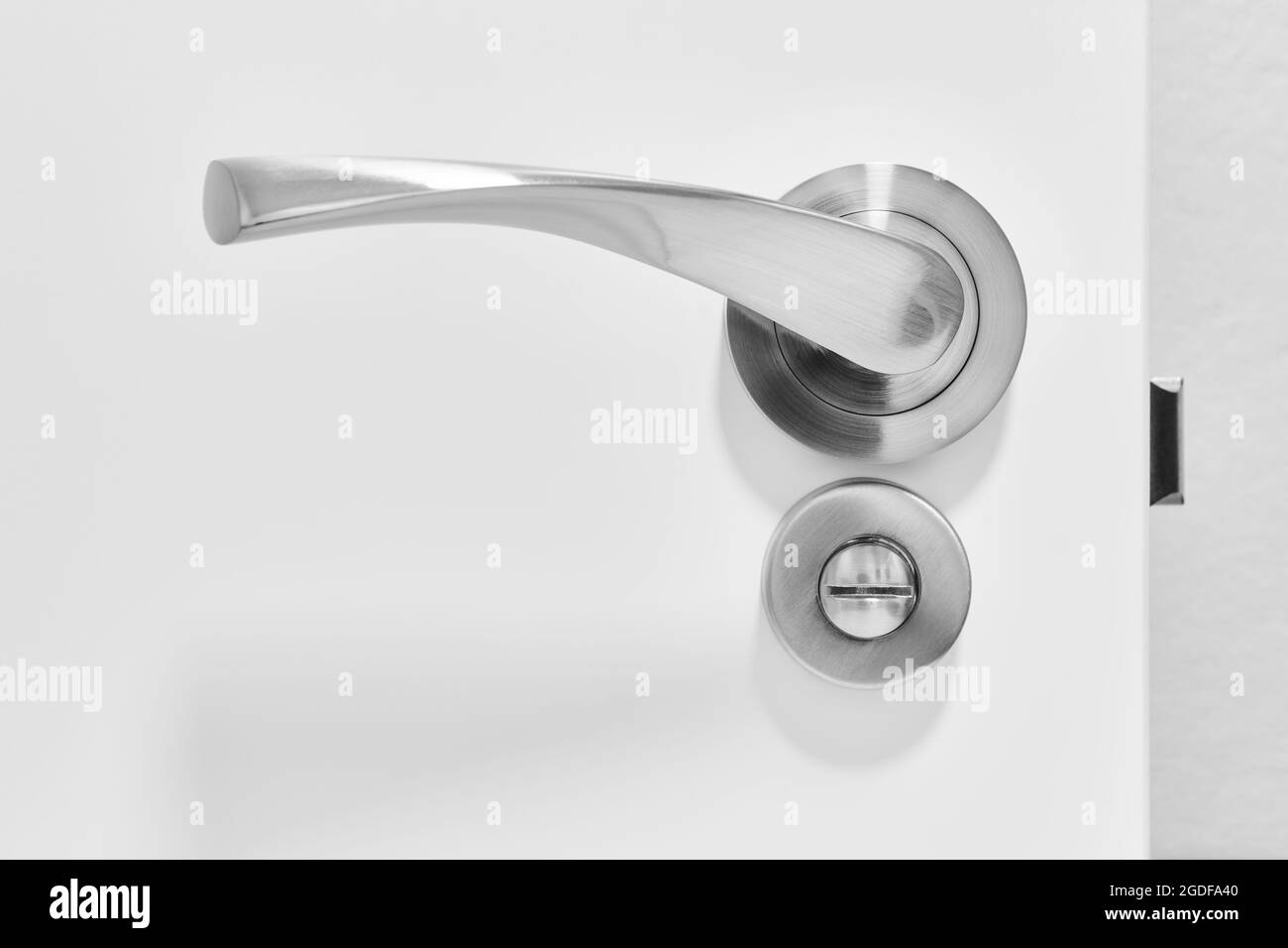 Metallic doorknob and bolt on a white wooden door. Detail Stock Photo