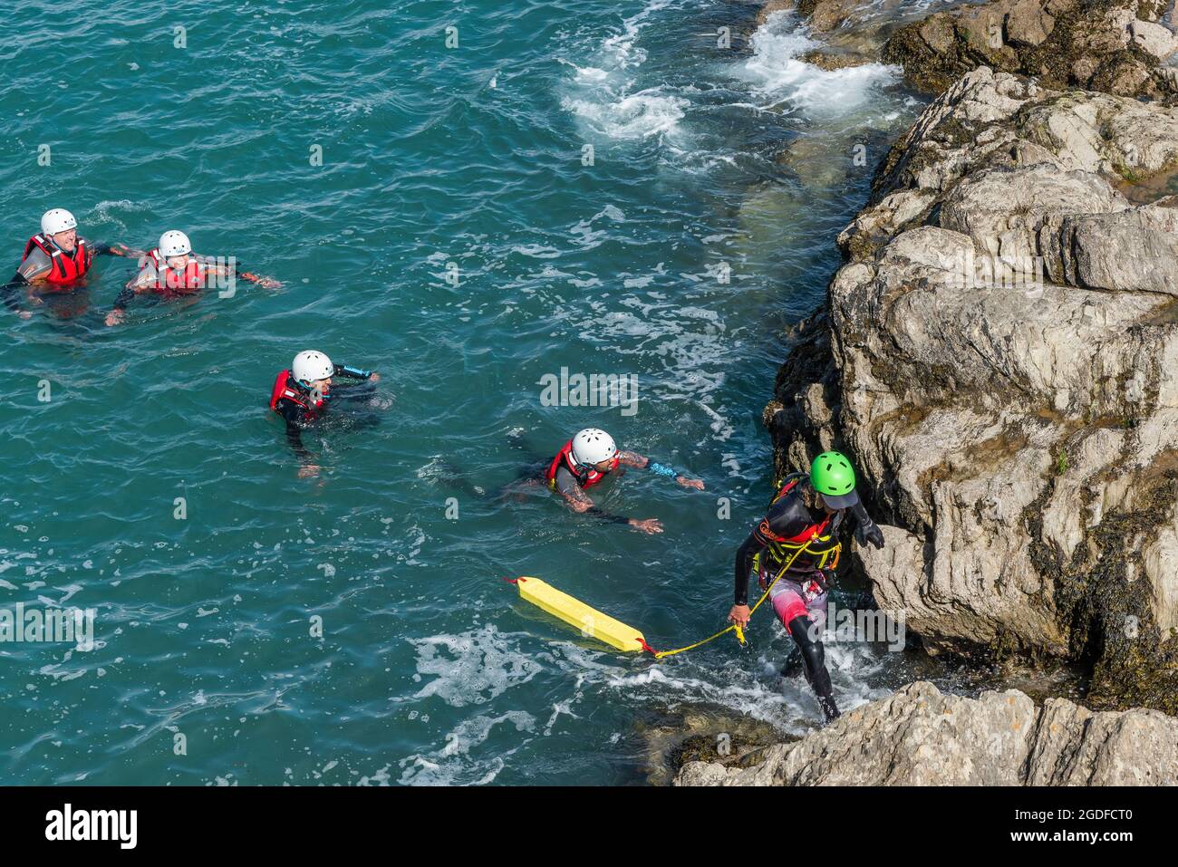 Holidaymakers and their guide swimming in the sea on a coasteering adventure on Towan Head in Newquay in Cornwall. Stock Photo