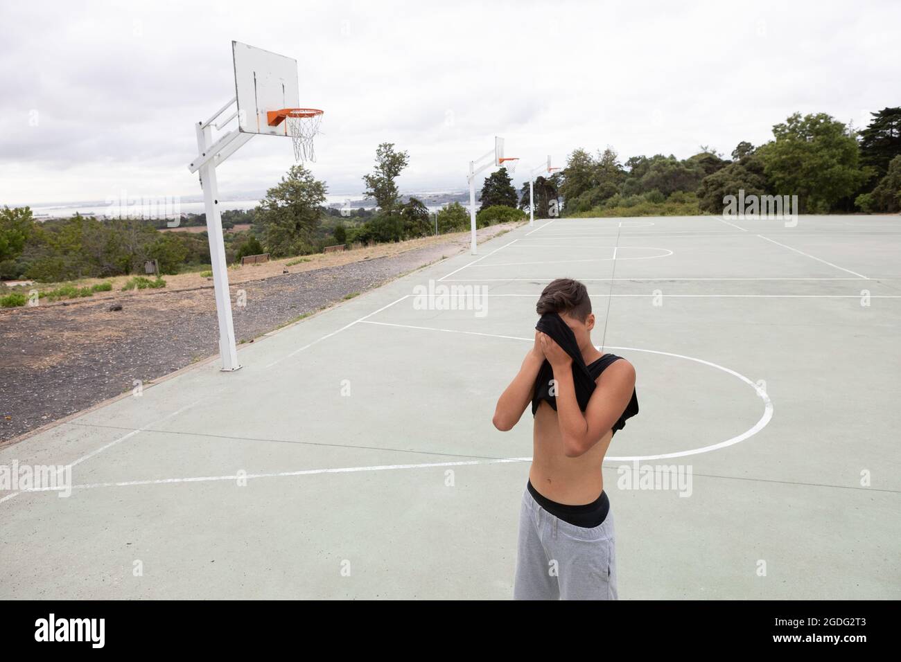 Male teenage basketball player wiping his brow with vest on basketball court Stock Photo