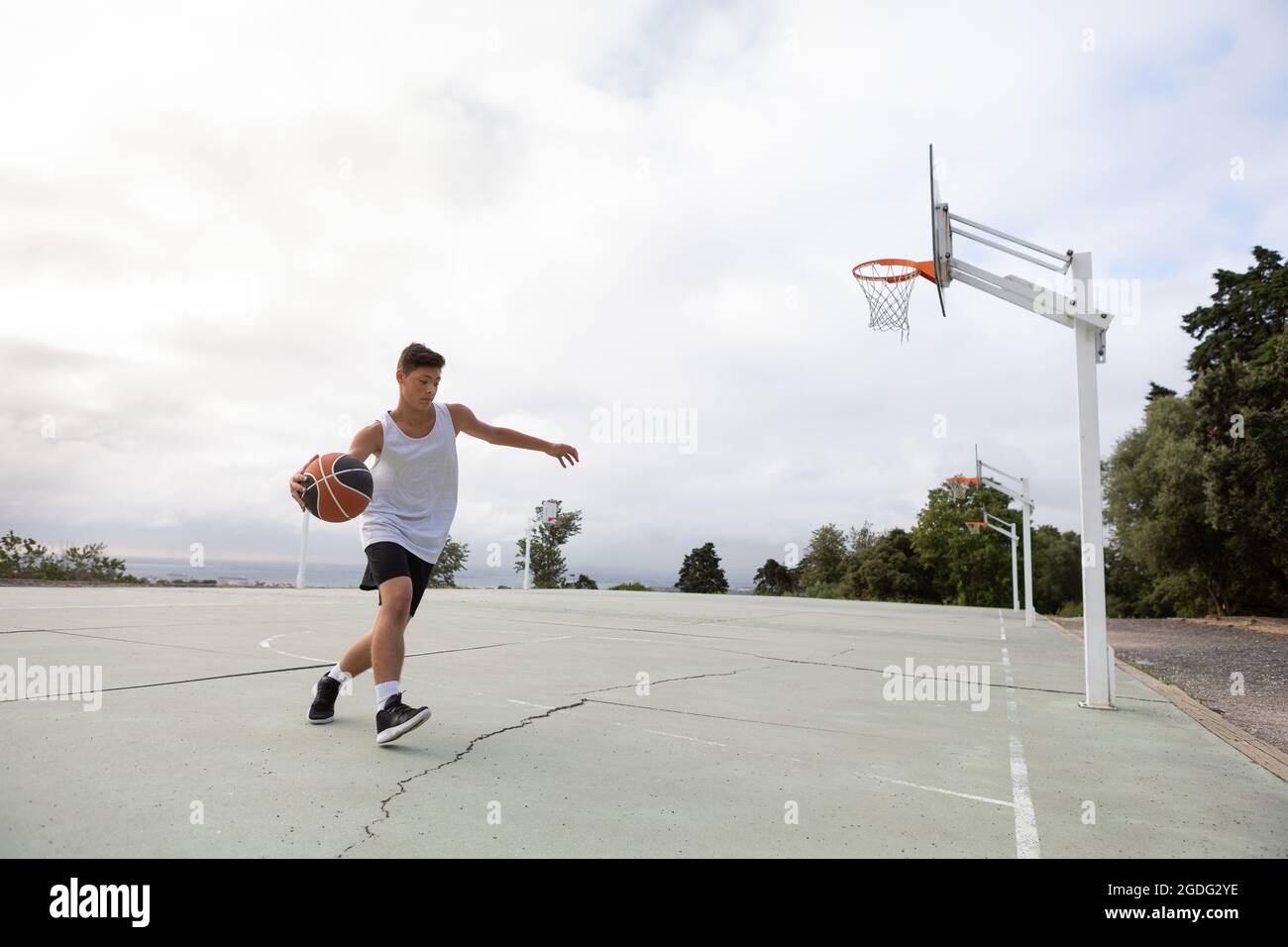 Male teenage basketball player running with ball on basketball court Stock Photo