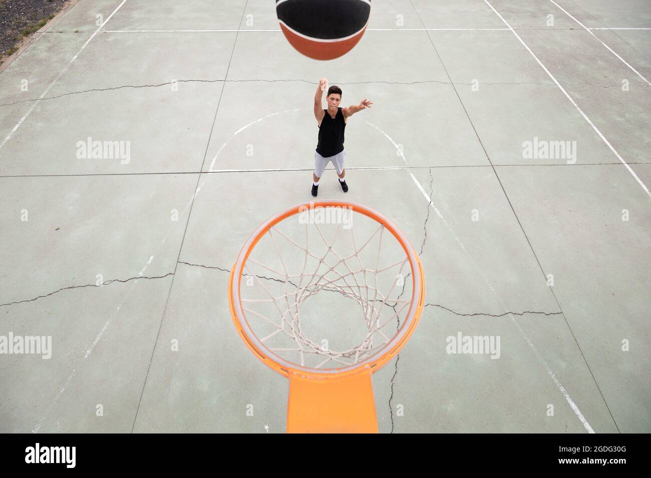 Male teenage basketball player throwing ball toward basketball hoop