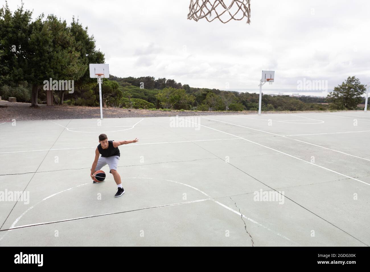 Male teenage basketball player practicing with ball near basketball