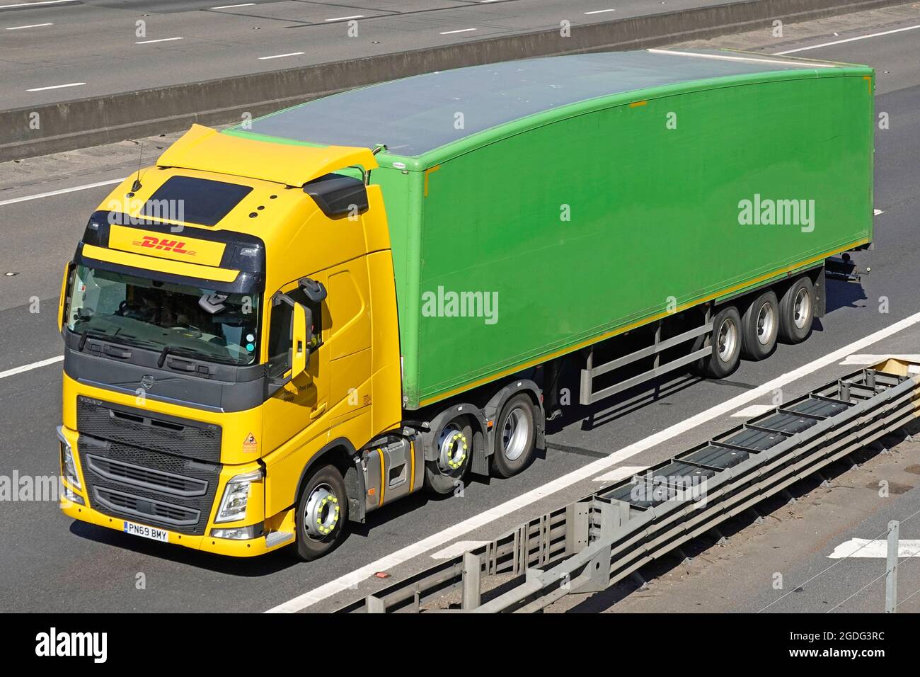 Front side & view hgv lorry truck operated by DHL a courier package delivery & express mail business towing a green unmarked articulated trailer UK Stock Photo