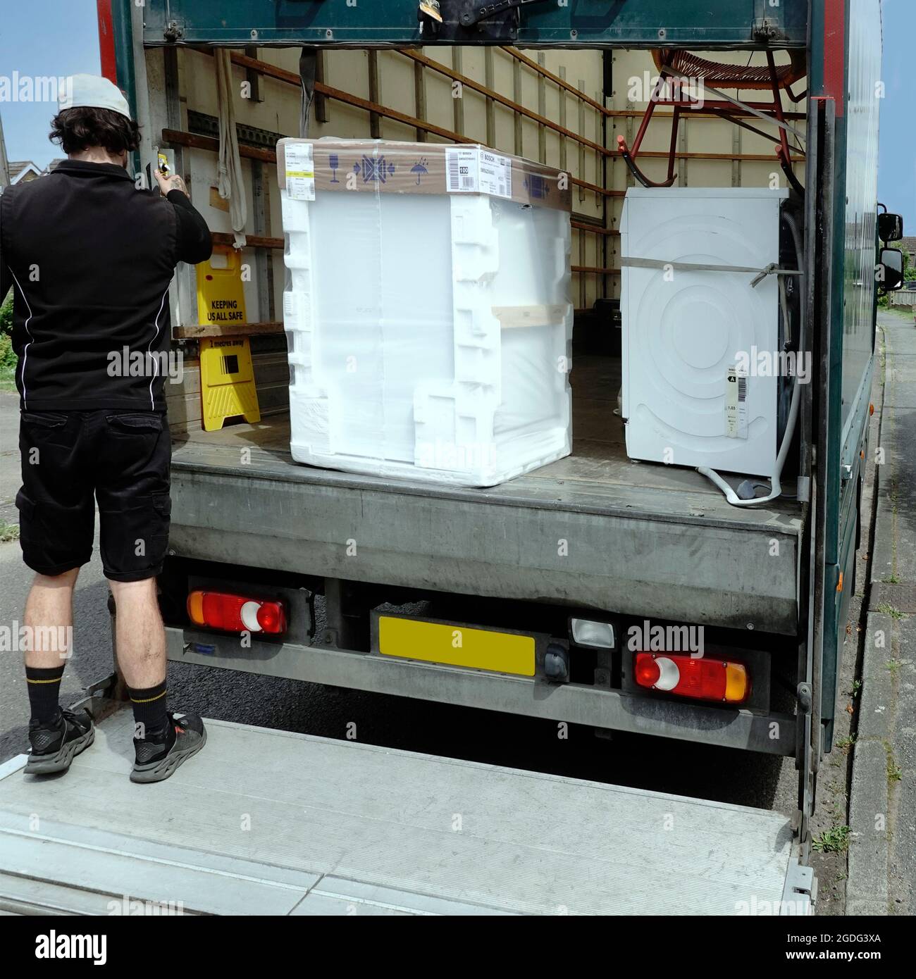 John Lewis department store home delivery driver on lorry tailgate for new Bosch white goods domestic dishwasher appliance in polystyrene packaging UK Stock Photo