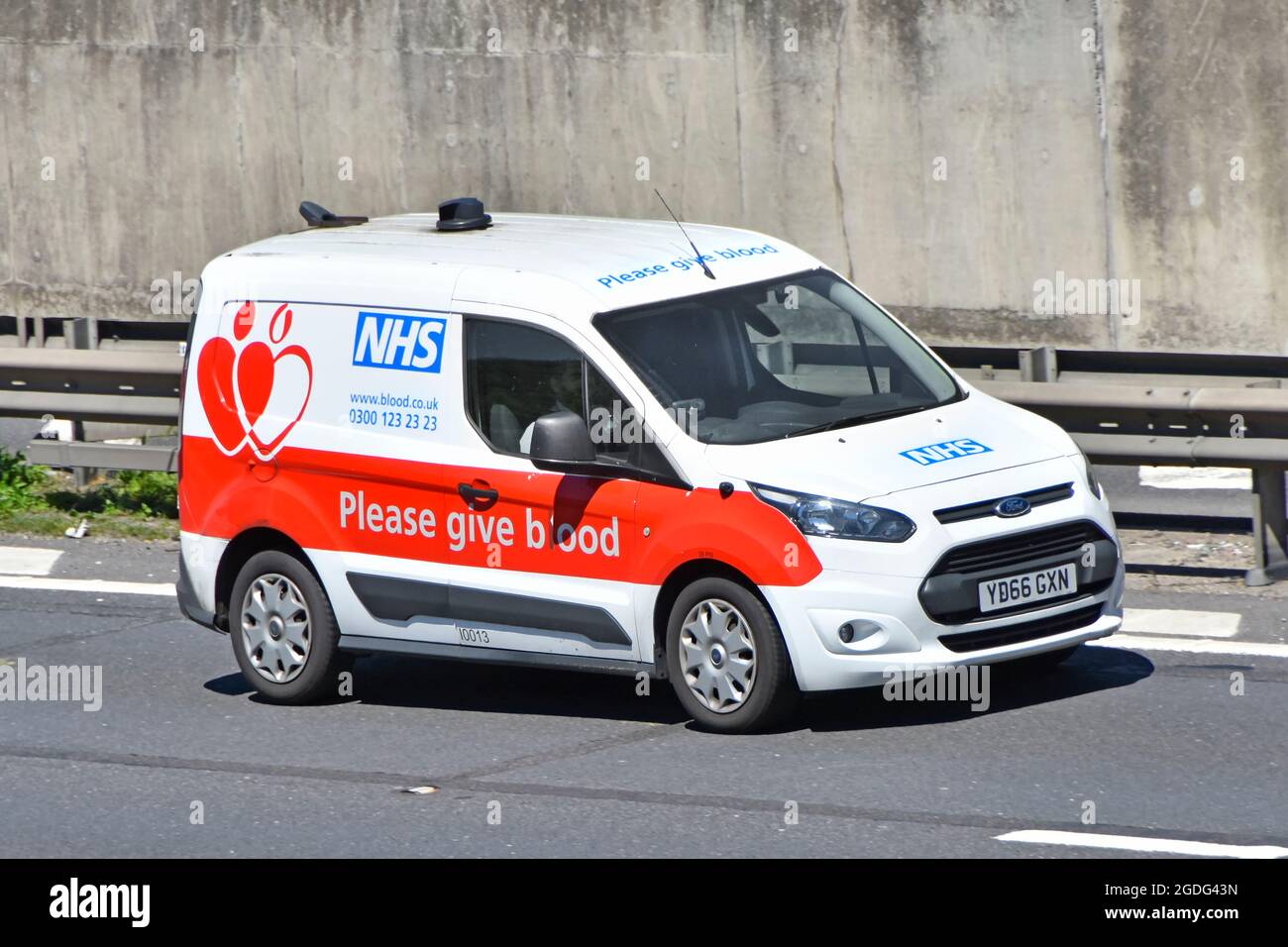 Front view of National Health Blood Transfusion Service NHS Ford van give blood graphics on side of vehicle driving along motorway road England UK Stock Photo