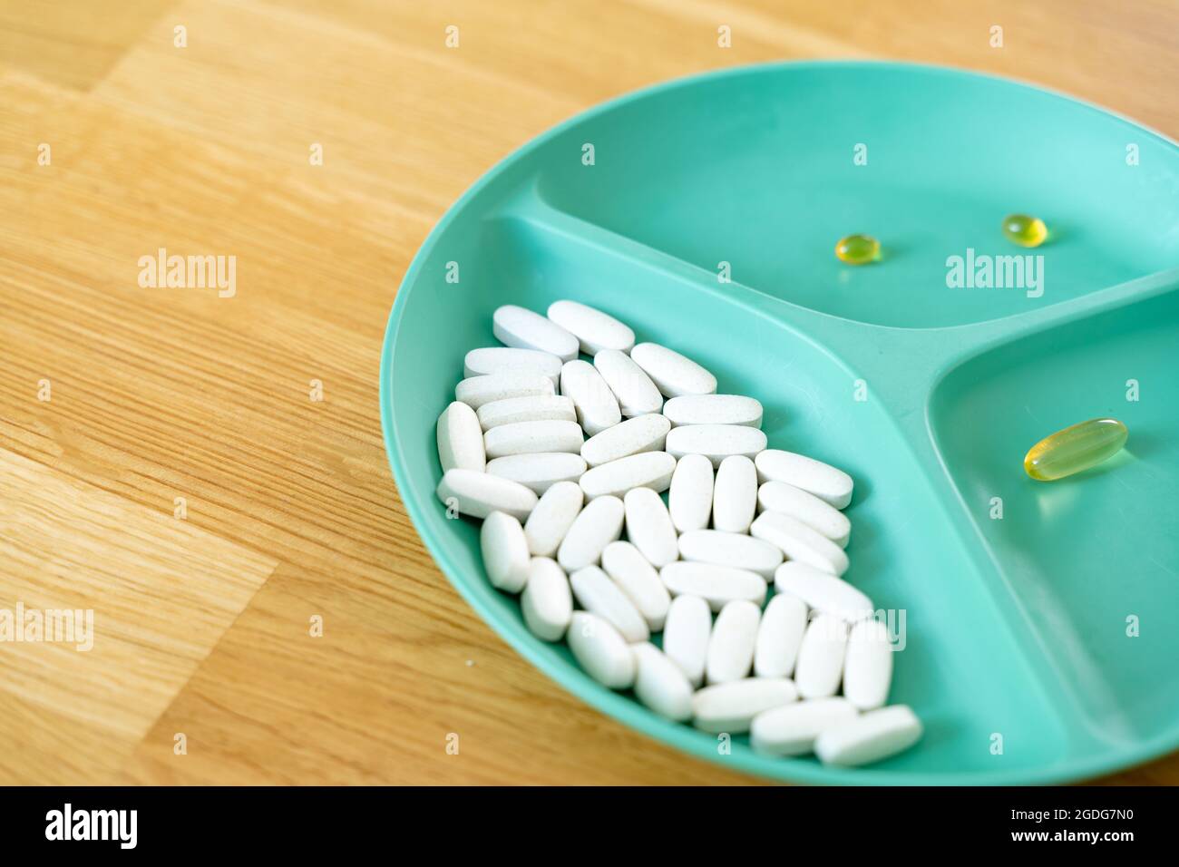 Green plate with dividers filled with pills and capsules. Biohacking movement. Wellbeing concept. Modern medicine with antibiotics. Stock Photo