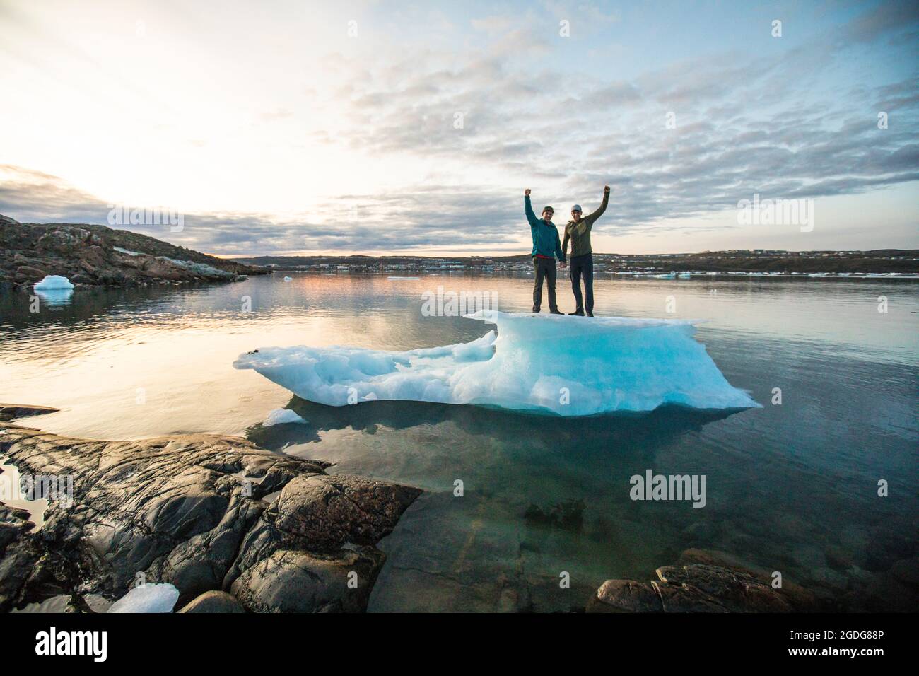 Couple standing on iceberg with arms raised in celebration Stock Photo