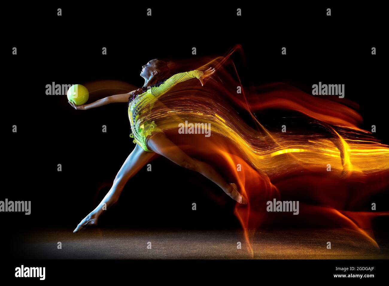 Portrait of young girl, rhythmic gymnastics artist in action isolated on dark studio background with mixed light. Concept of sport, action, aspiration Stock Photo