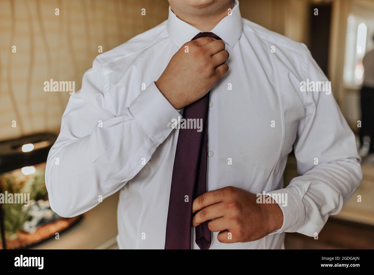 an adult man in a white strict shirt straightens his tie with his hands at home Stock Photo