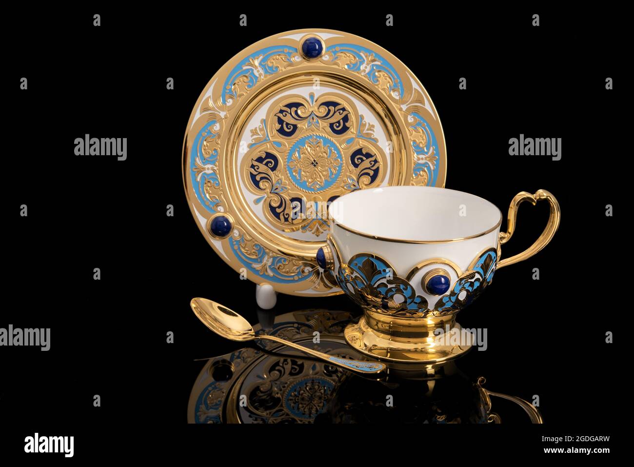 Luxury gold Tea party kit. Cup, plate, and spoon. isolated on black background with reflection. Souvenir gift with traditional patterns. Stock Photo