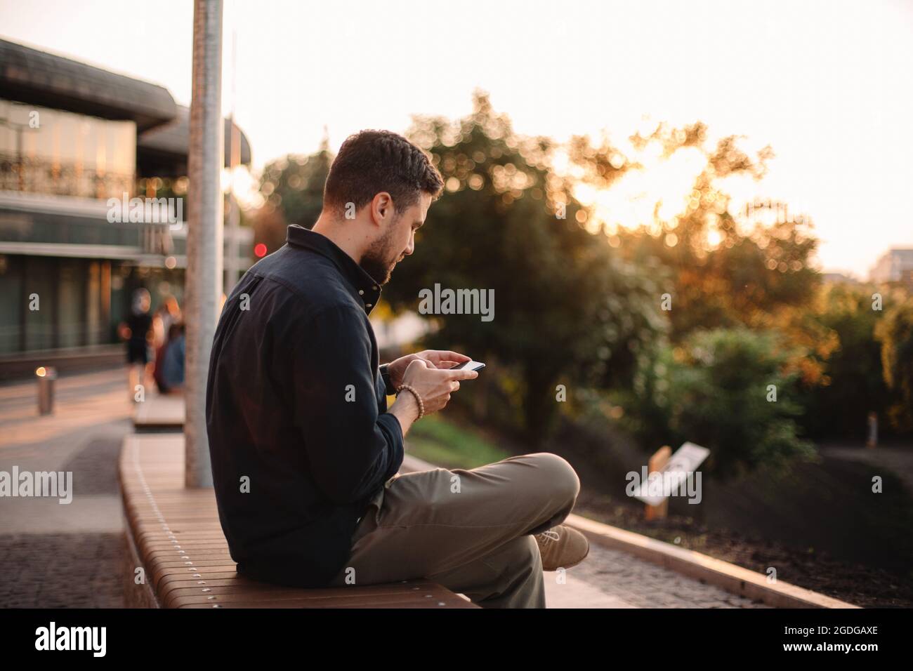Happy man using smart phone sitting on bench at sunset Stock Photo