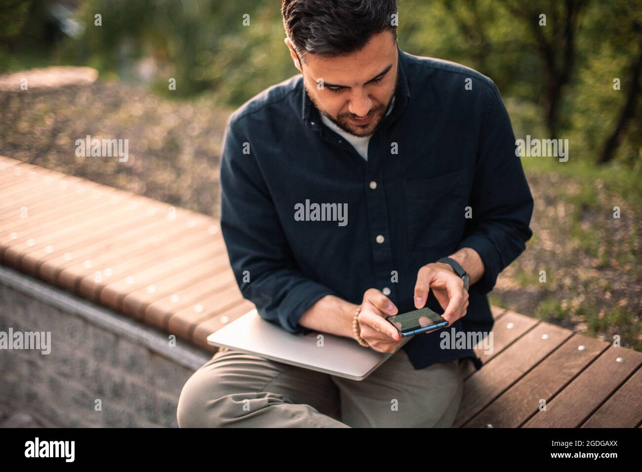 businessman using smart phone while sitting on bench in park Stock Photo
