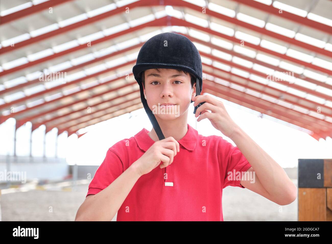 Teenage boy putting a riding helmet on his head and looking at camera. Stock Photo