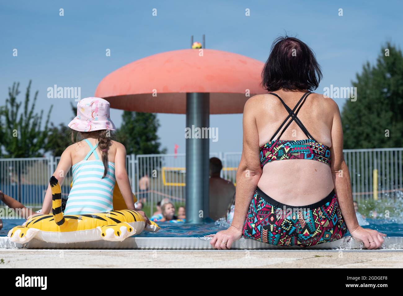 Dresden, Germany. 13th Aug, 2021. Bathers sit at the edge of a pool in