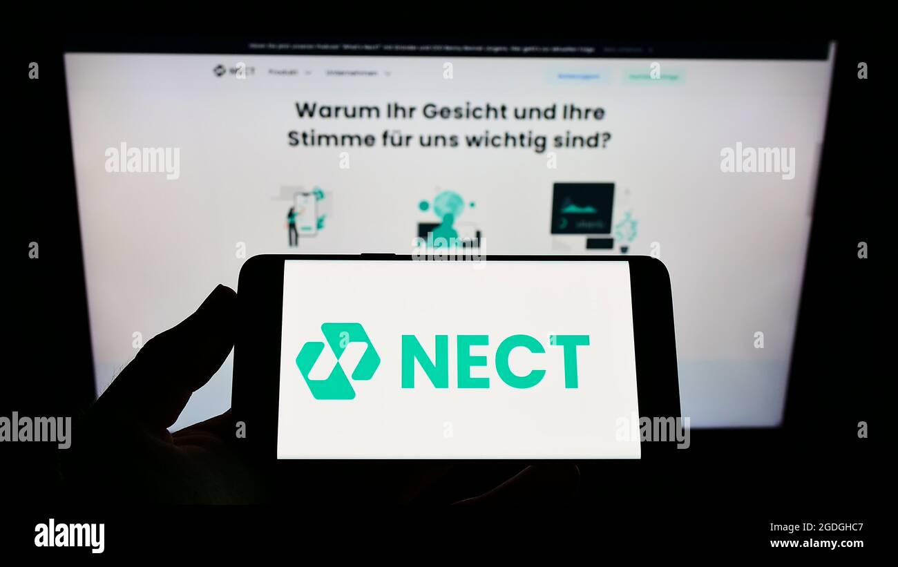 Person holding cellphone with logo of German identity verification company Nect GmbH on screen in front of business webpage. Focus on phone display. Stock Photo