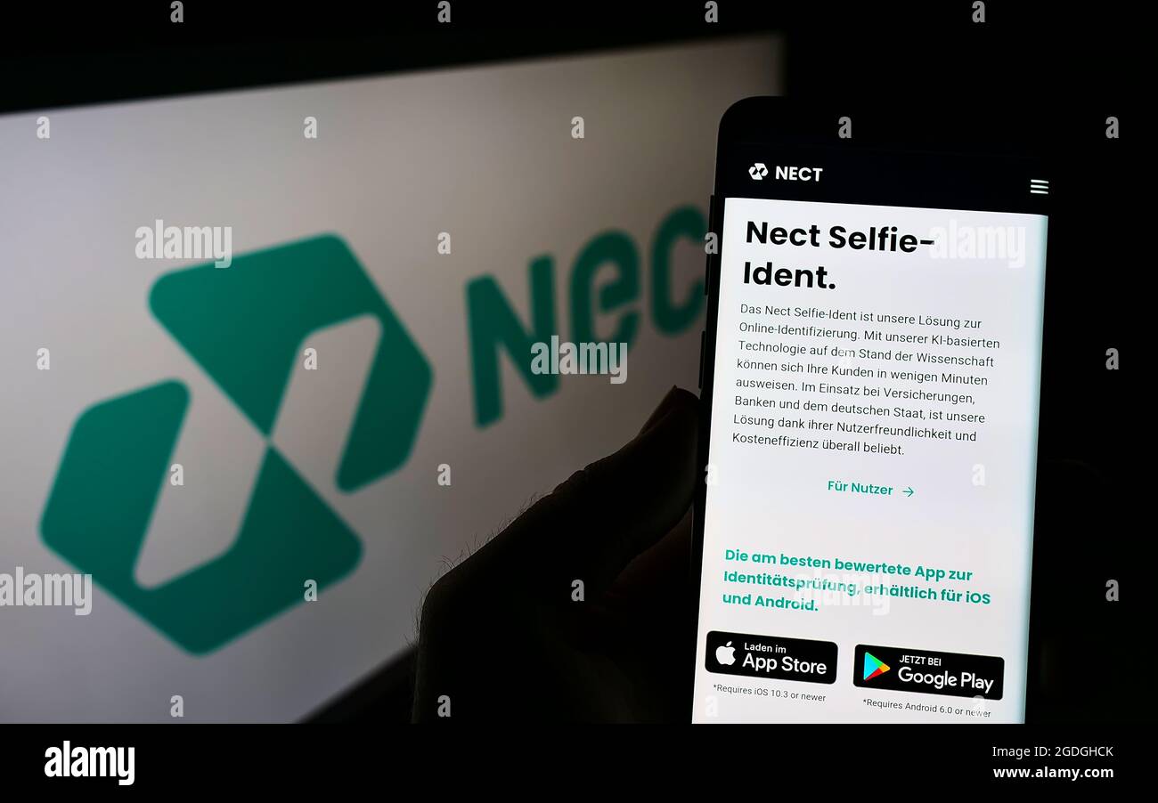 Person holding mobile phone with webpage of German identity verification company Nect GmbH on screen with logo. Focus on center of phone display. Stock Photo