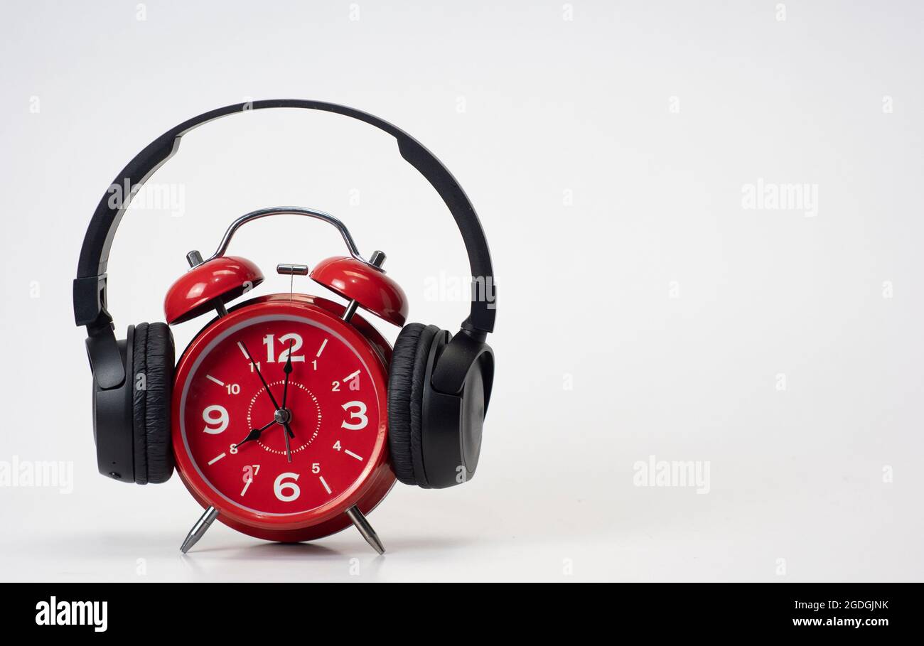 Red Alarm Clock put on headphones over white background, Timeless Music Concept. Copy space Stock Photo