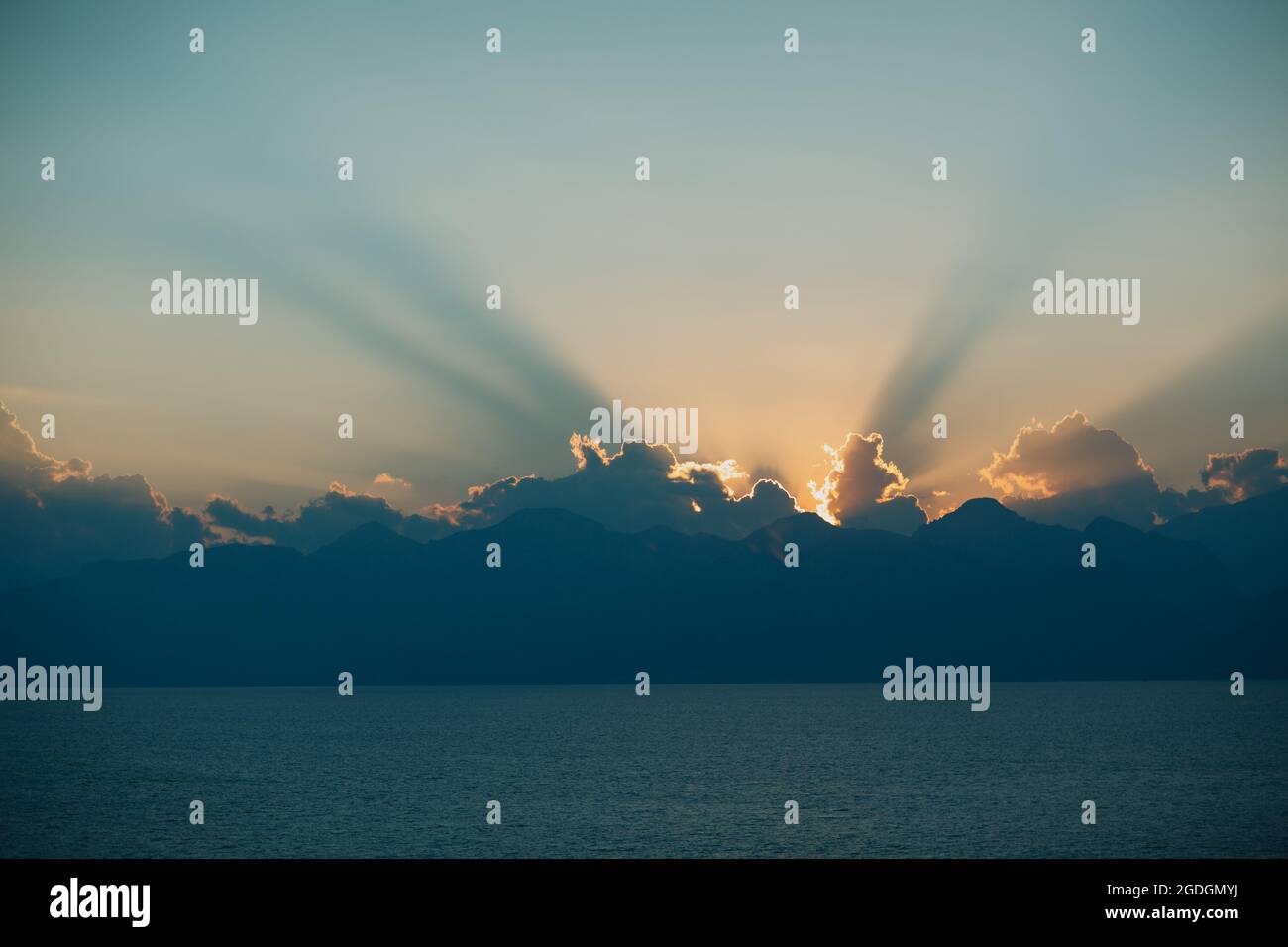 Dramatic sun rays through cloudy dark sky against sunset ocean. Stock Photo