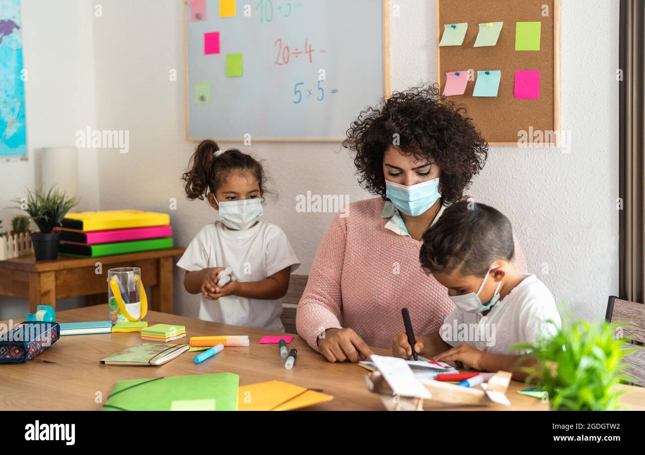 Female teacher with children drawing in preschool classroom while wearing face protective mask