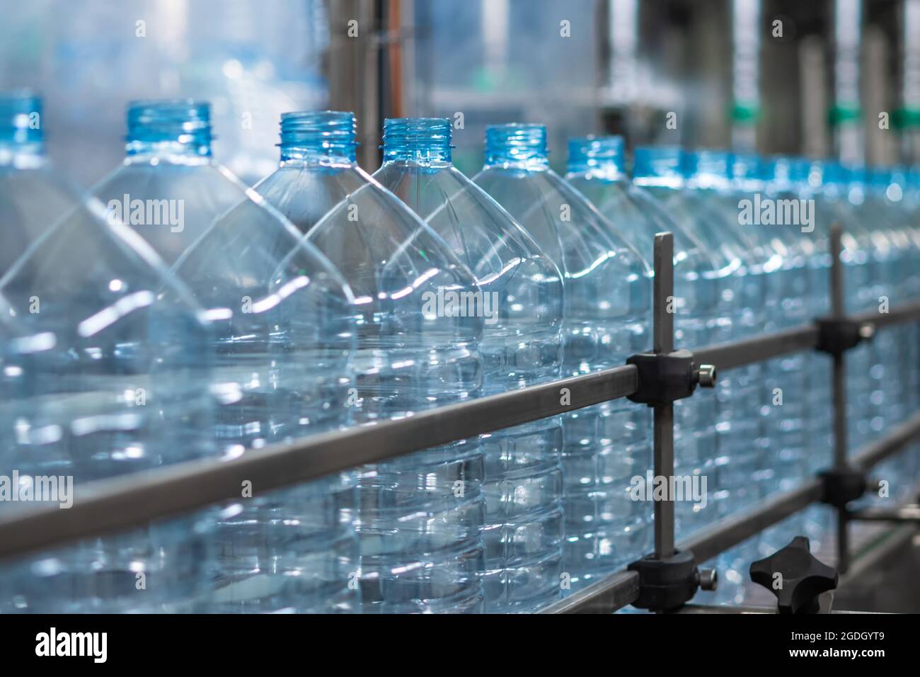 Empty blue five-liter plastic bottles on a conveyor belt. Automated production of drinking water. Food production Stock Photo