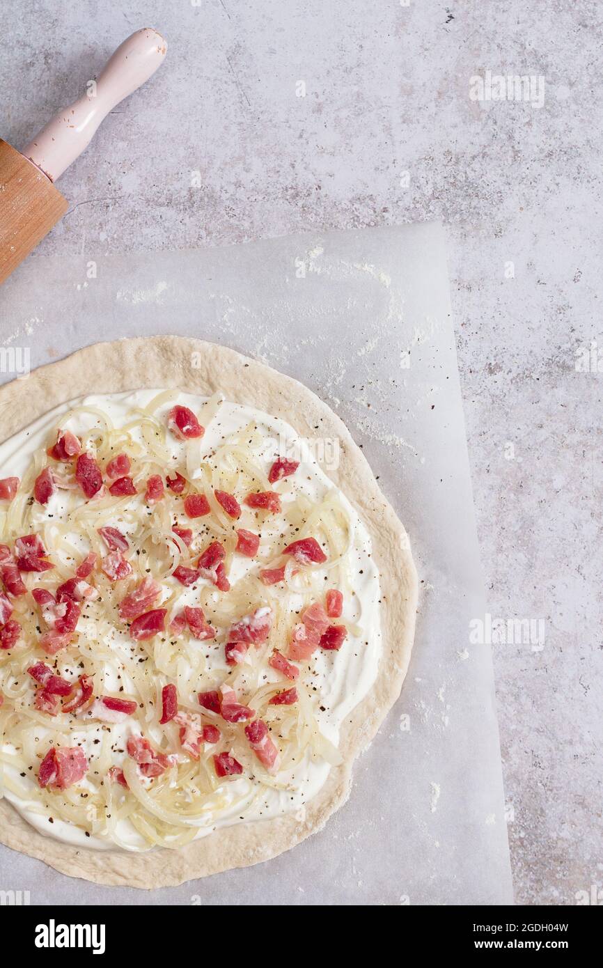 Preparation of a tarte flambee (flammkuchen) with creme fraiche, fromage blanc, lardons and onions. Stock Photo