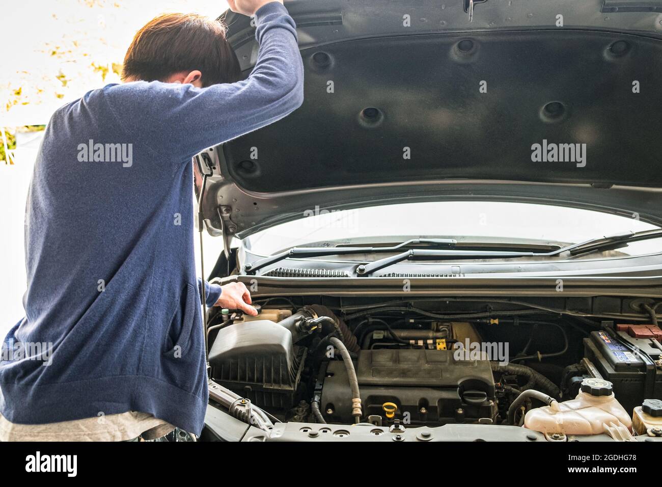 Young man checking liquid car in front engine and raising car hood ...
