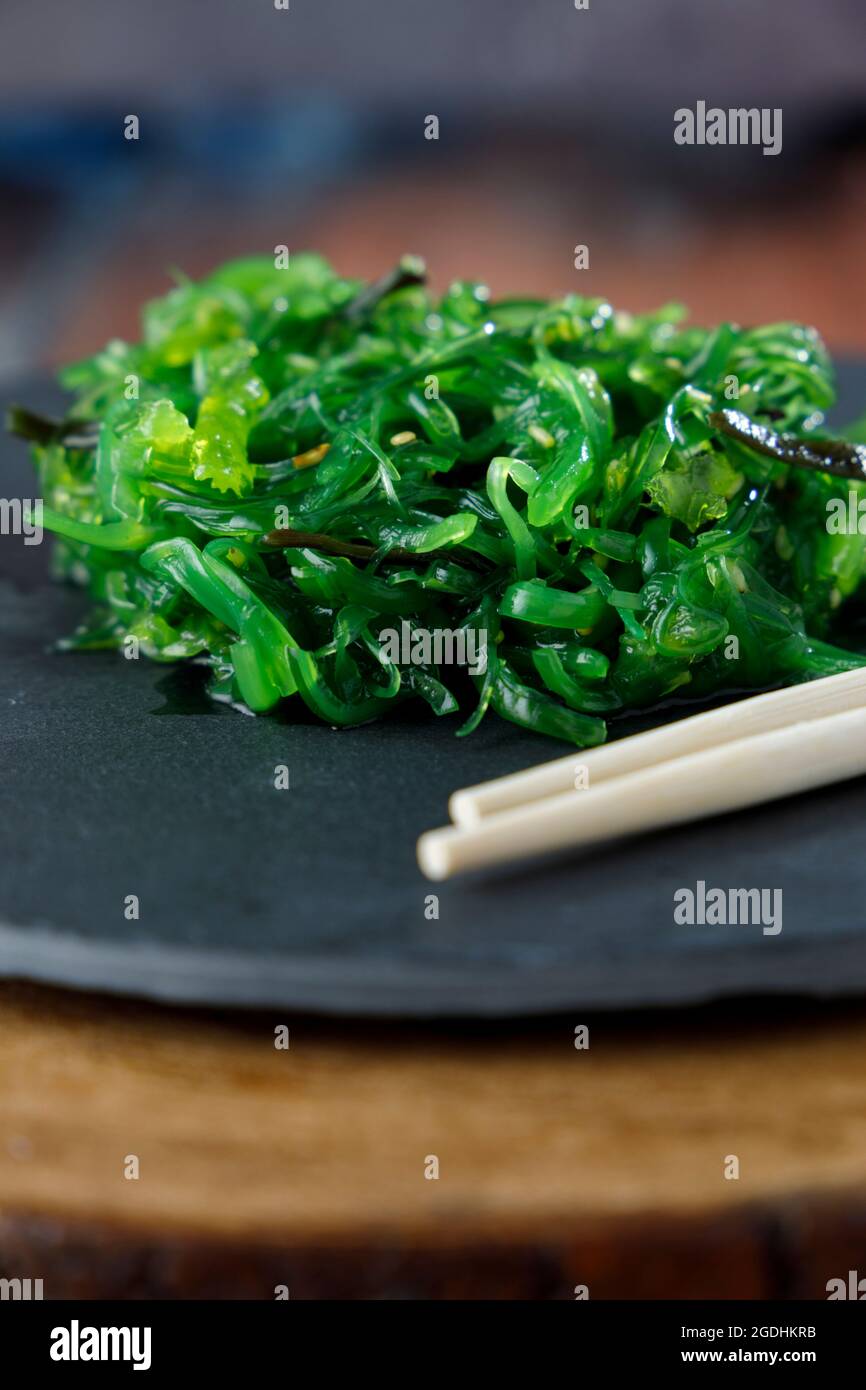 Wakame seaweed salad with sesame on black plate and wooden table Stock Photo