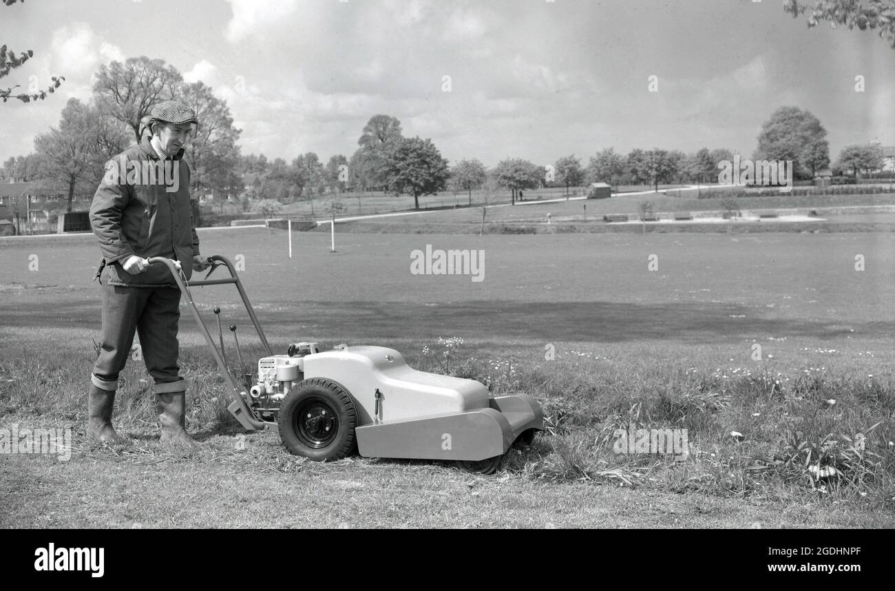 1960s, historical, a groundsman in wellington boots, jacket and cloth cap using a lawnmower, petrol driven with four-wheels, to cut long grass on rough ground. Made by Allen of Oxford, England, UK, the rotary mower is powered by a Briggs & Stratton aluminum engine.  Founded in the USA in 1908, Briggs & Stratton was providing power for numerous agricultural applications by the 1920s and in 1953, revolutionised the lawn and garden industry by developing the first lightweight aluminum engine, vastly improving the ease of use of rotary lawn mowers. Stock Photo