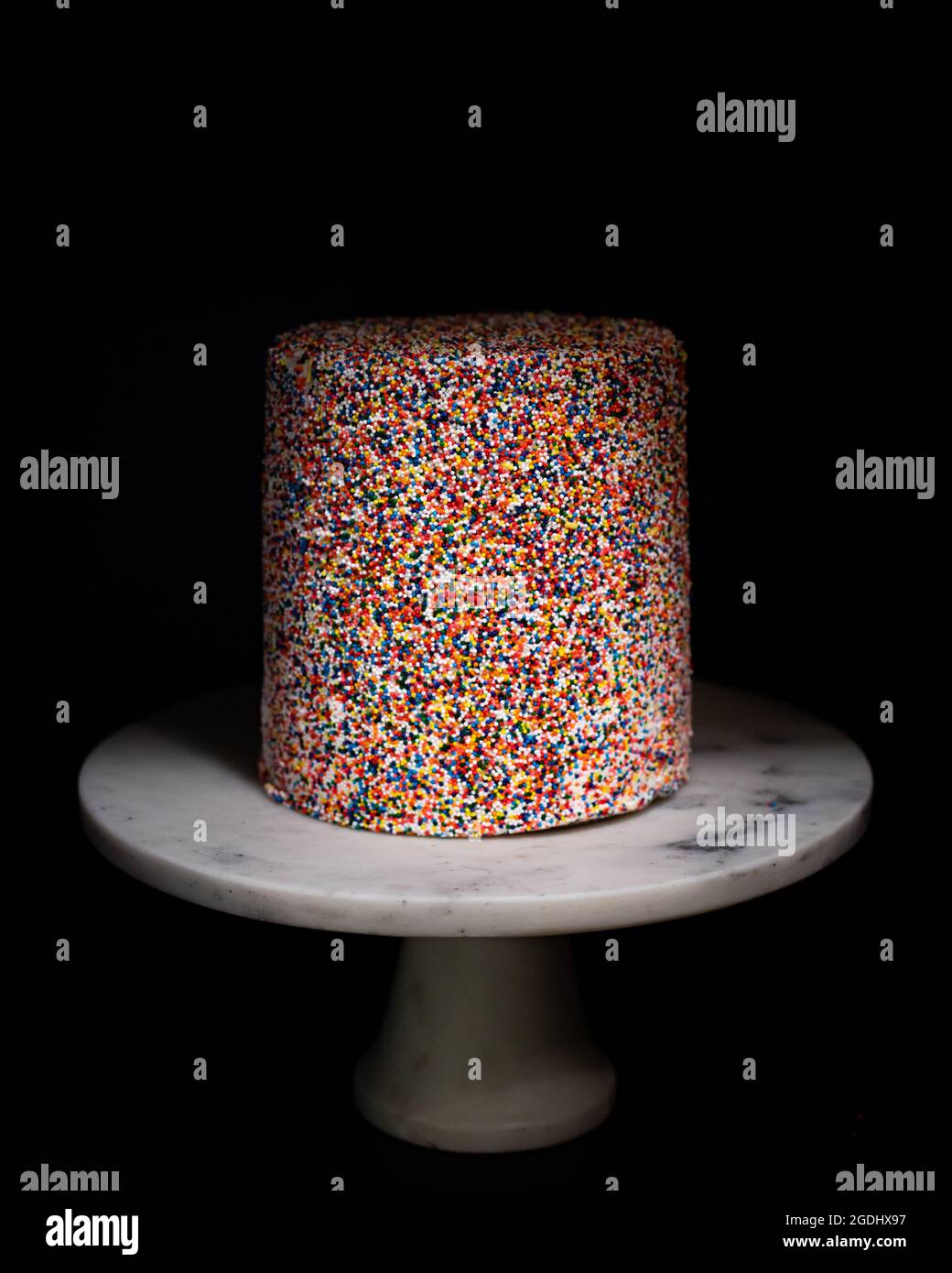 rainbow sprinkle cake on white marble cake stand Stock Photo