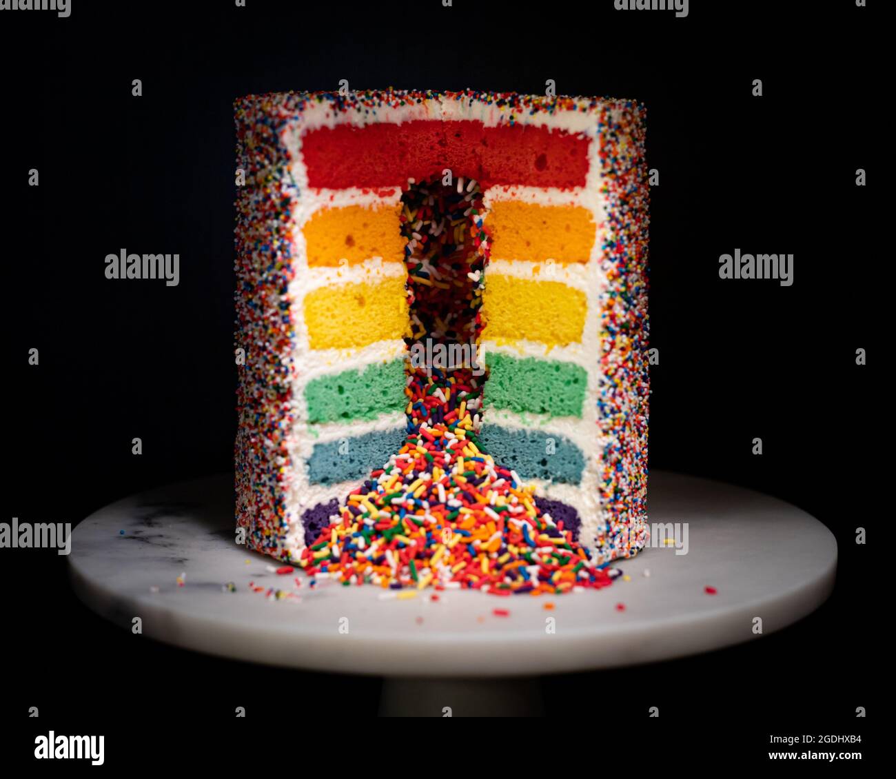 rainbow sprinkle layer cake on white marble cake stand Stock Photo