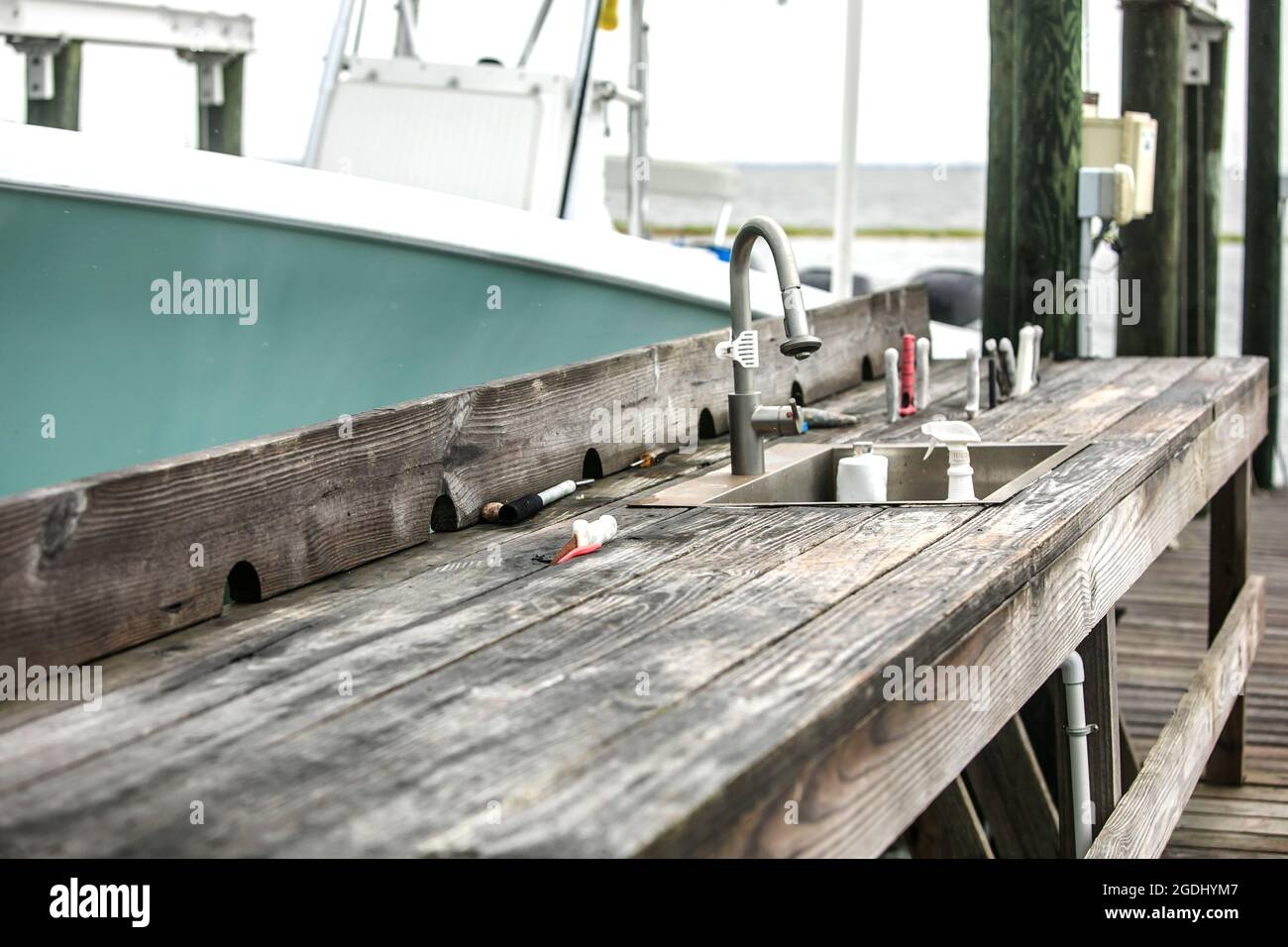 An old rustic and worn wood fish cleaning station on the dock of a pier  with a boat nearby Stock Photo - Alamy