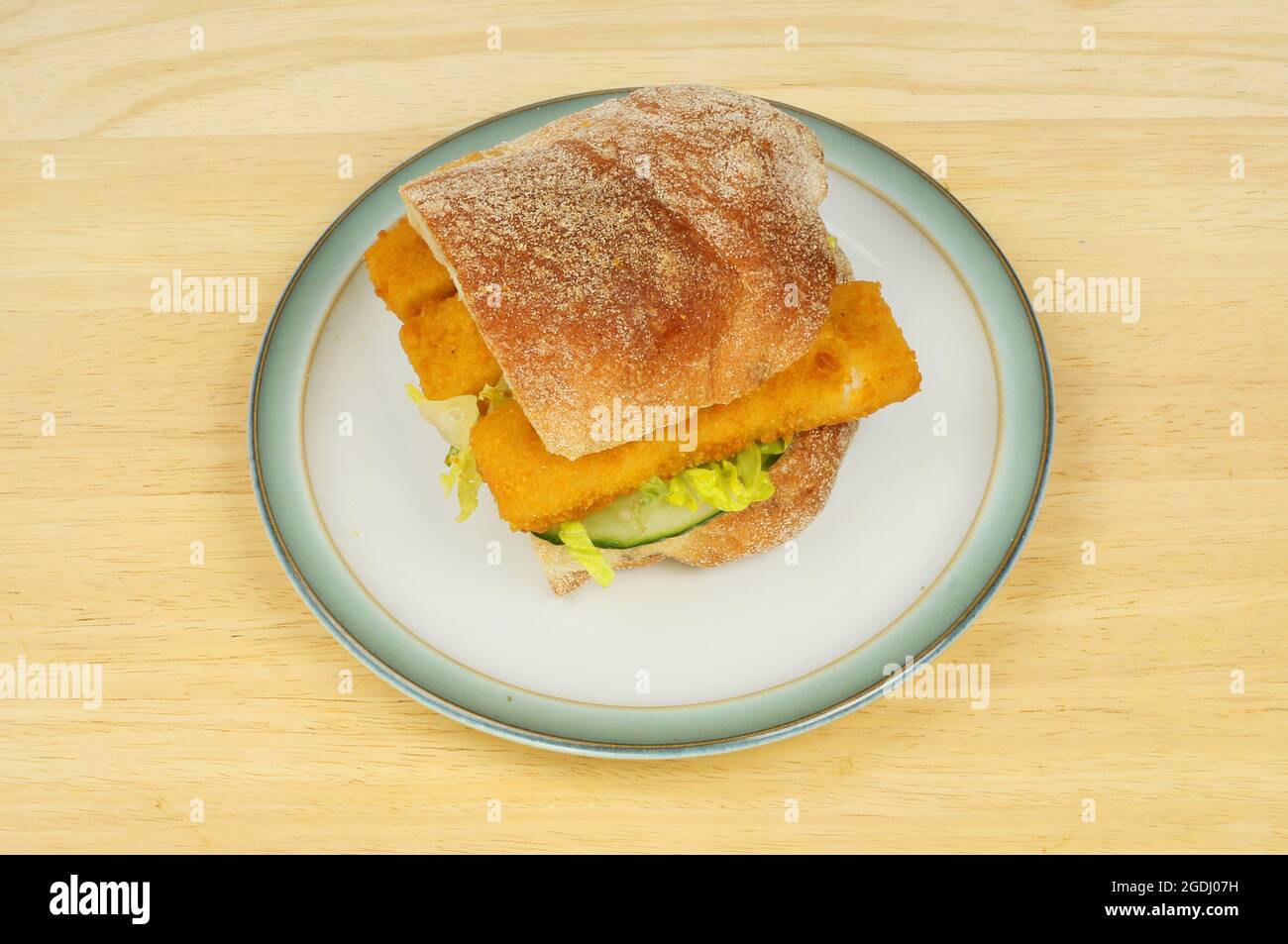 Fish fingers and salad in a ciabatta roll on a plate on a wooden tabletop Stock Photo