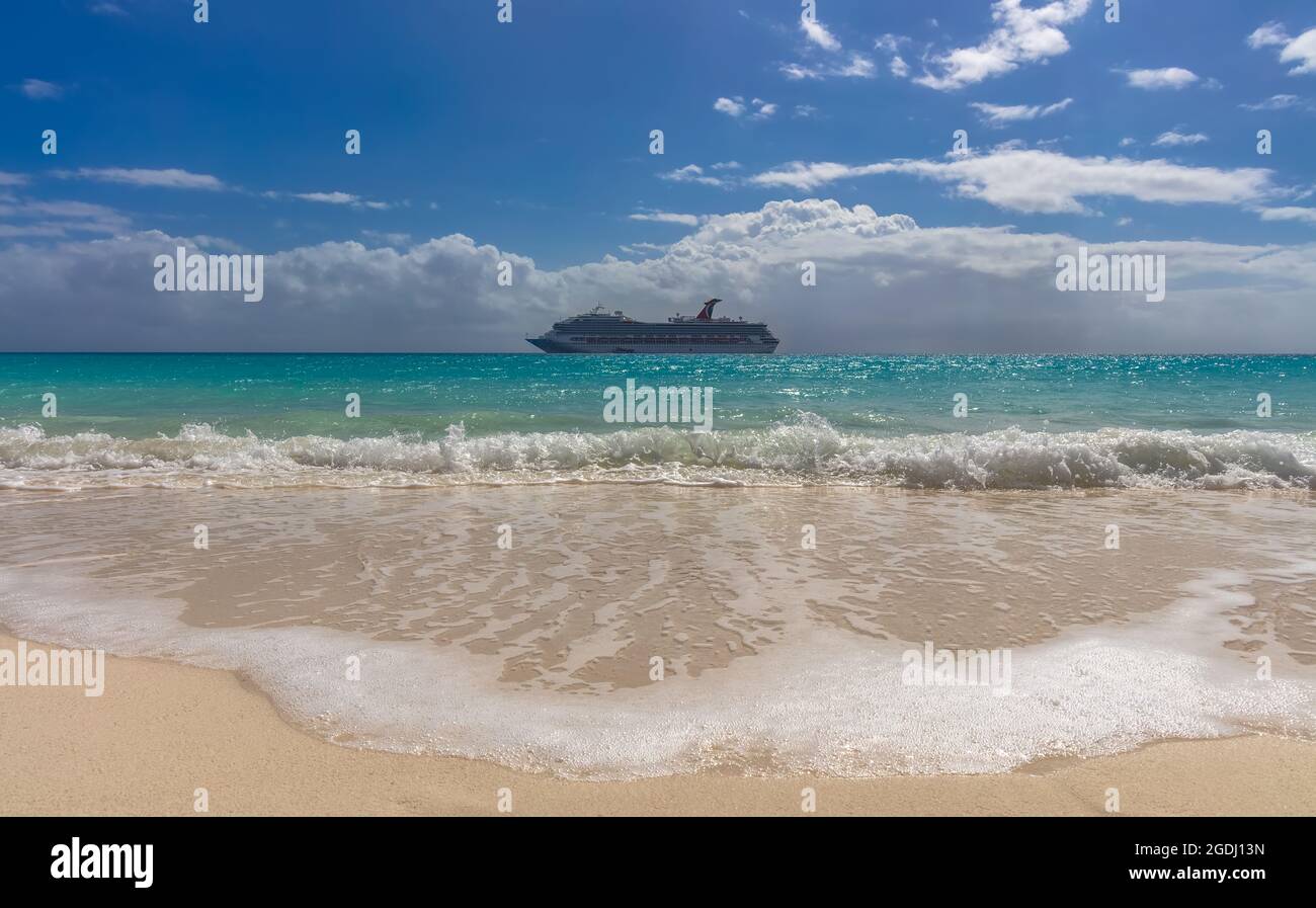 Half Moon Cay, Bahamas - February 19, 2020: Carnival Freedom anchoring by Half Moon Cay island. Gorgeous turquoise water splashing in the foreground. Stock Photo