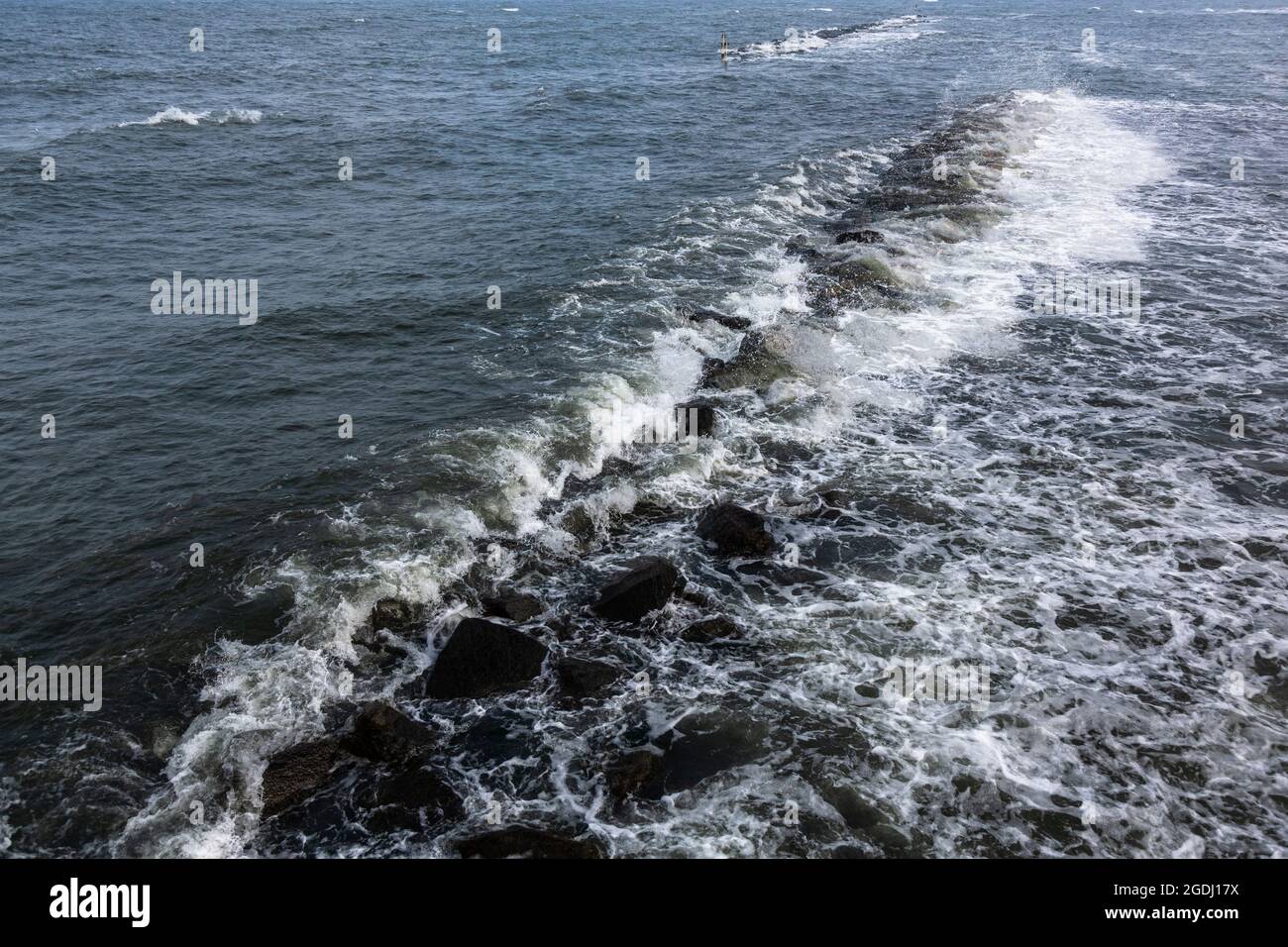 The Baltic Sea water washes over a breakwater made of stones and forms agitated and calm water. Stock Photo