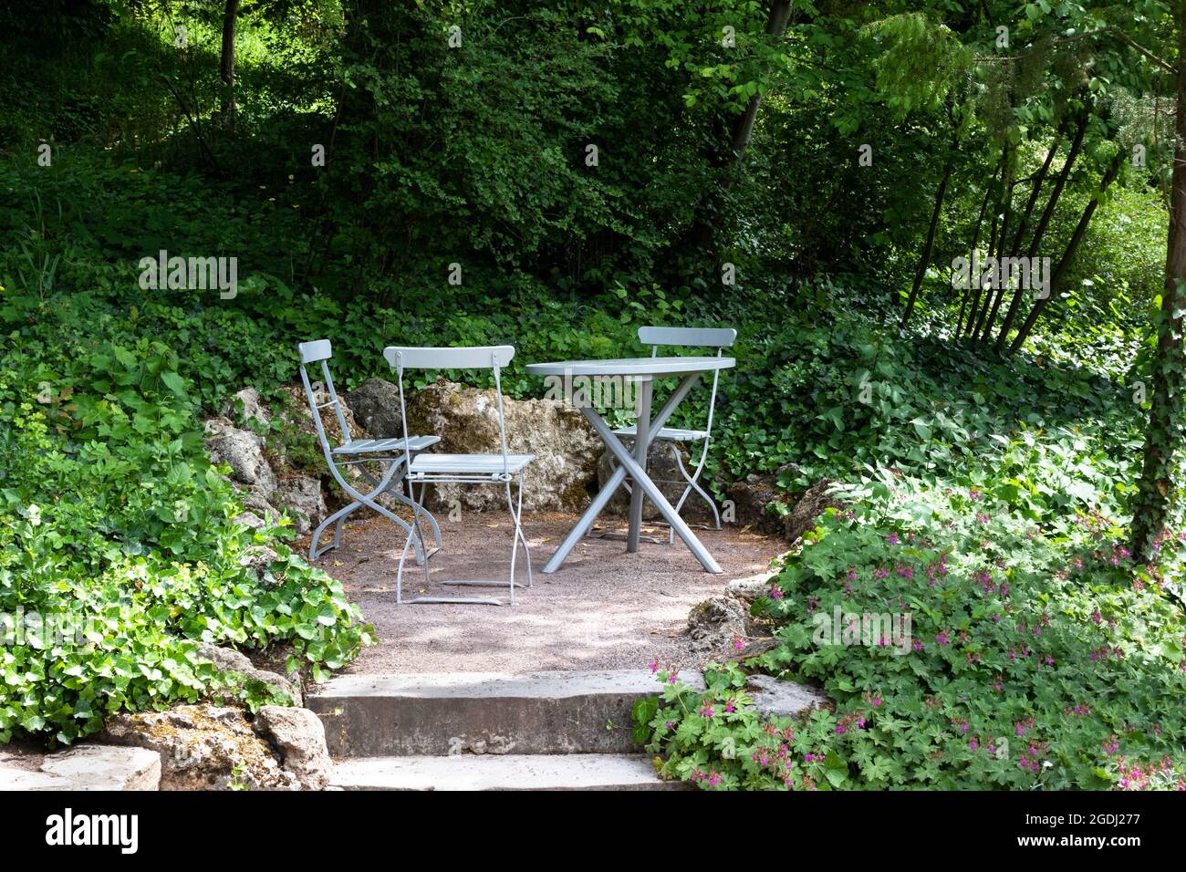 A cozy sitting area in the garden with folding chairs and a table in the shade of trees. Stock Photo