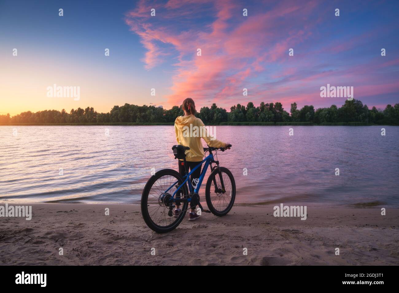 Woman with mountain bike on the river coast at sunset Stock Photo