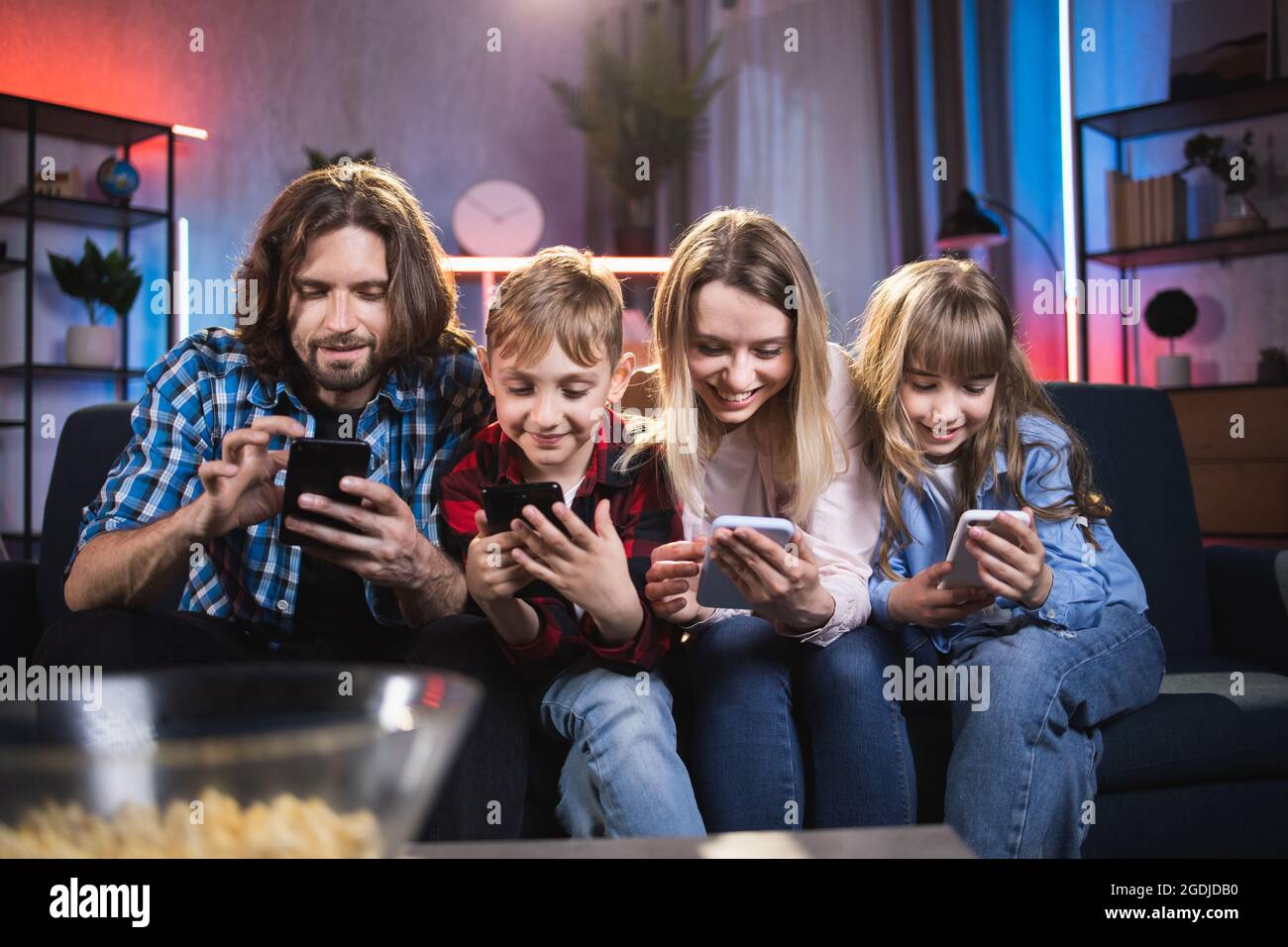 https://c8.alamy.com/comp/2GDJDB0/two-kids-and-their-parents-using-personal-smartphones-while-sitting-on-couch-smiling-family-with-gadgets-in-hands-spending-time-at-home-technology-and-people-concept-2GDJDB0.jpg