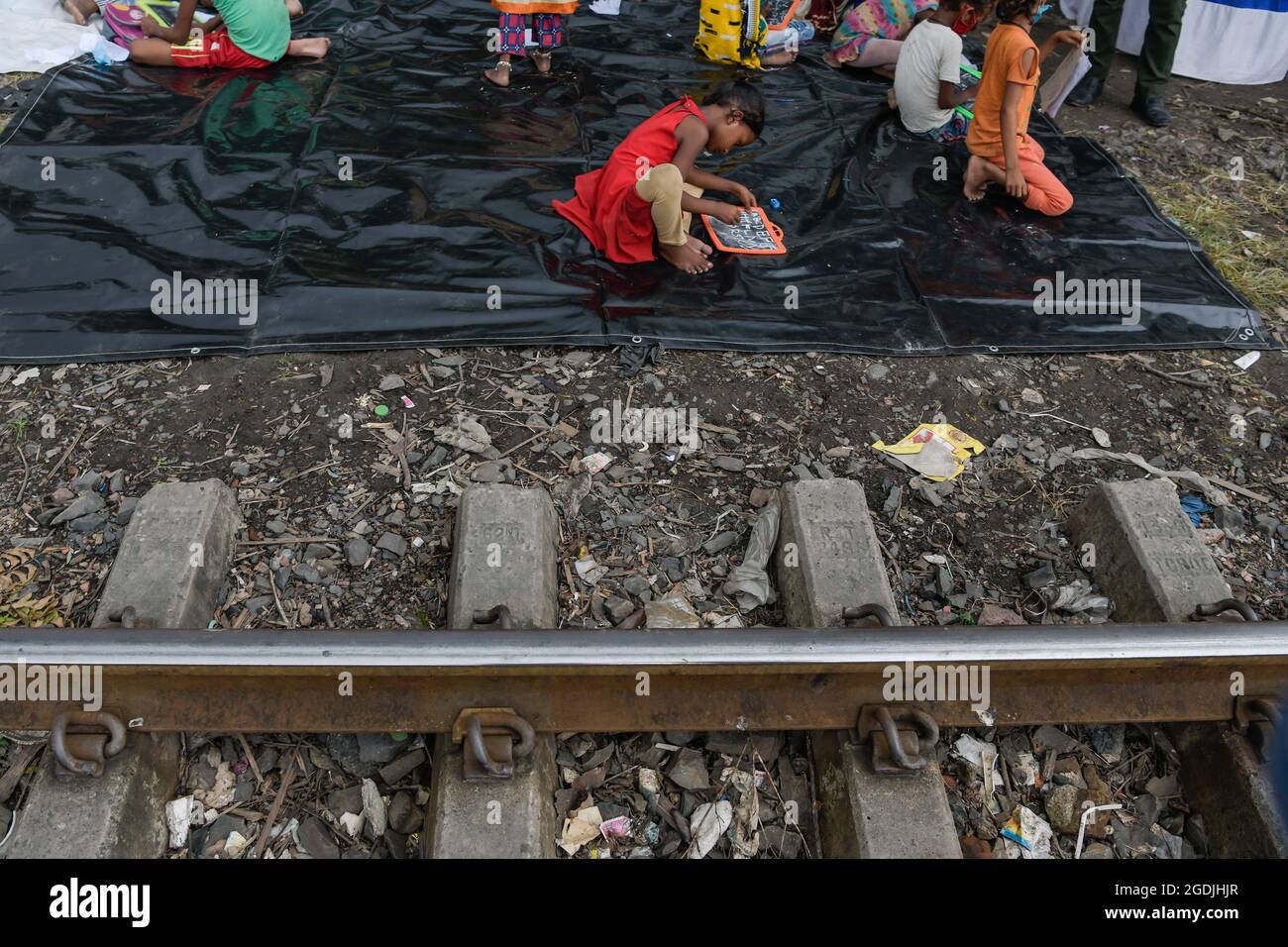 Kolkata, India. 13th Aug, 2021. A girl takes down notes during an interactive class organized by the South West Traffic guard beside a railway track at a slum in Kolkata.As educational institutions are closed for over a year now in India, the South West traffic guards have arranged special interactive classes beside a railway track for the underprivileged children at a slum in Kolkata, who have no access to online classes. Credit: SOPA Images Limited/Alamy Live News Stock Photo