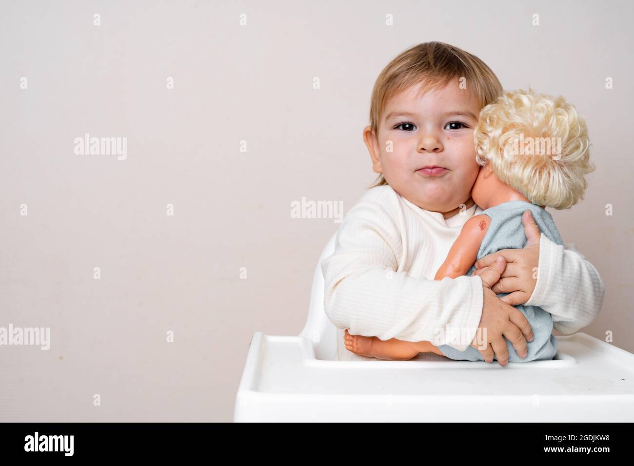 Baby toddler hugs with old-fashioned doll on a studio shot. Funny ...