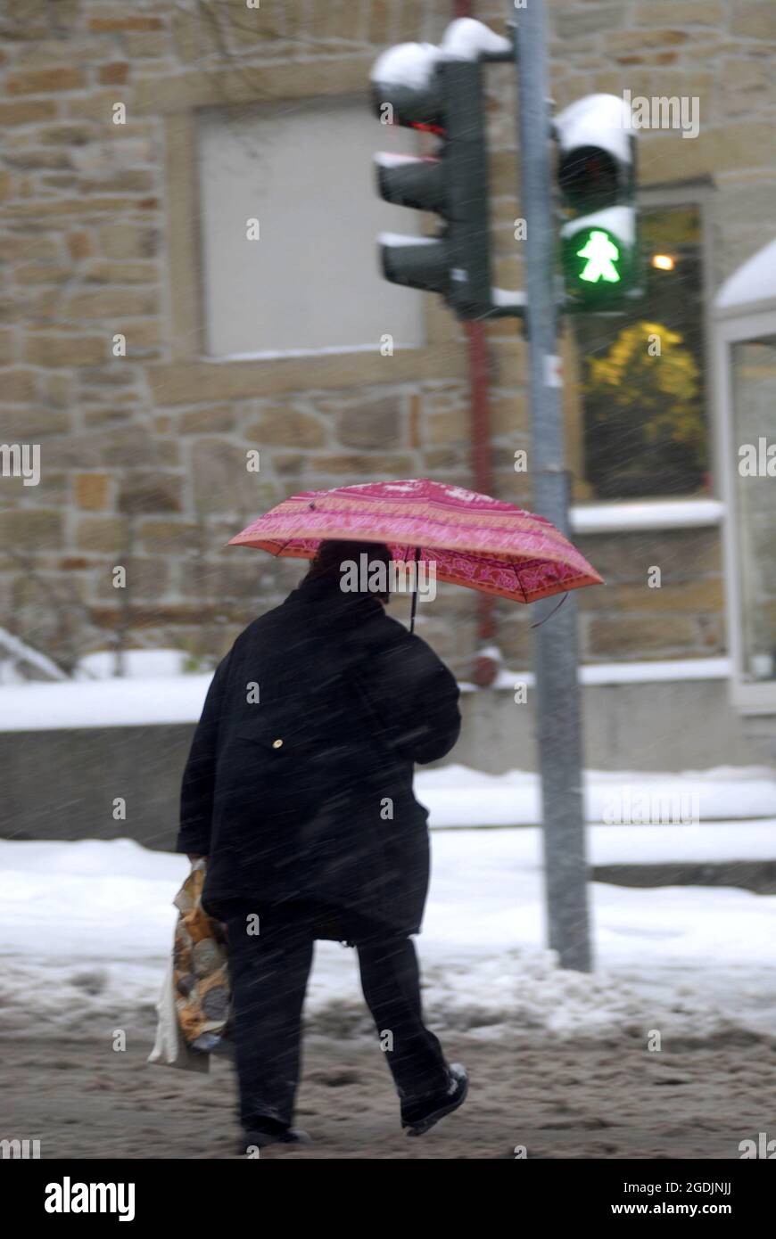 female pedestrian with umbrella walking in winter across the street at ...