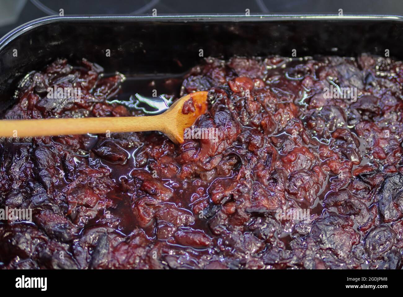 Preparation of plum jam at home in the kitchen, a wooden spoon mixes boiled plums Stock Photo