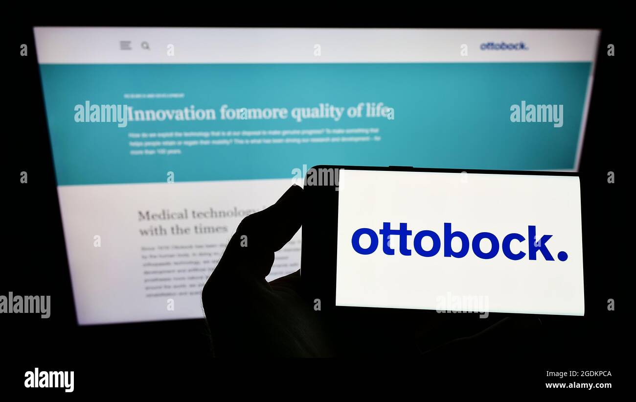 Person holding smartphone with logo of German prosthetics company Ottobock SE Co. KGaA on screen in front of website. Focus on phone display. Stock Photo