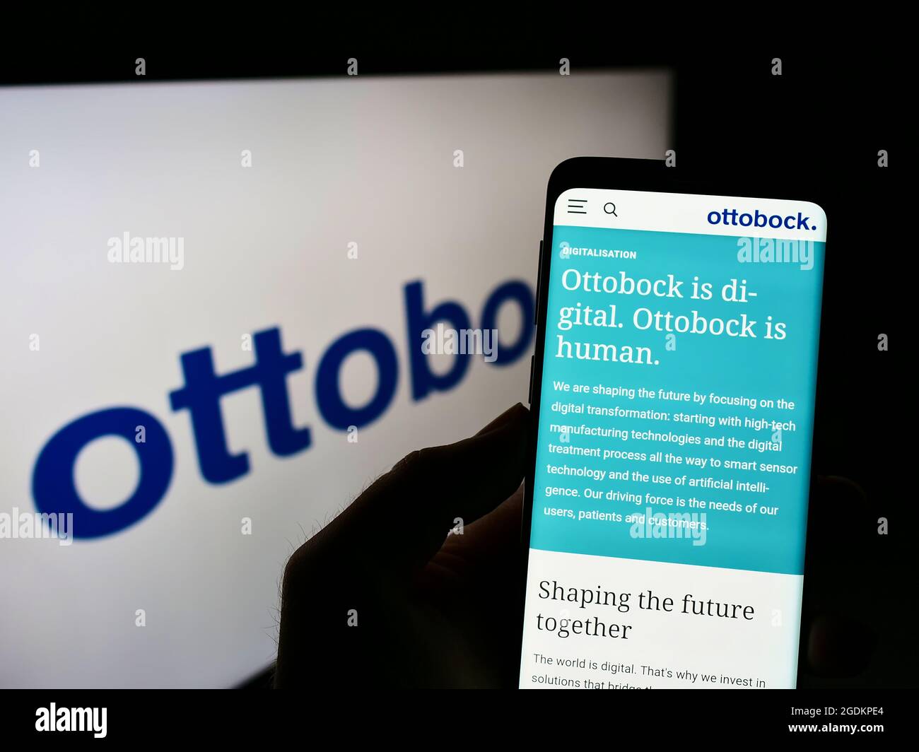 Person holding cellphone with webpage of German prosthetics company Ottobock SE Co. KGaA on screen with logo. Focus on center of phone display. Stock Photo