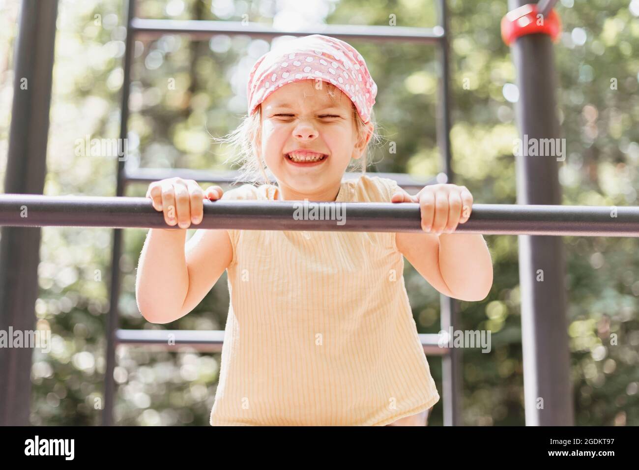 little girl pulls herself up on a horizontal bar in a city park on a
